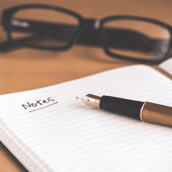 Notepad and pen with glasses in the background