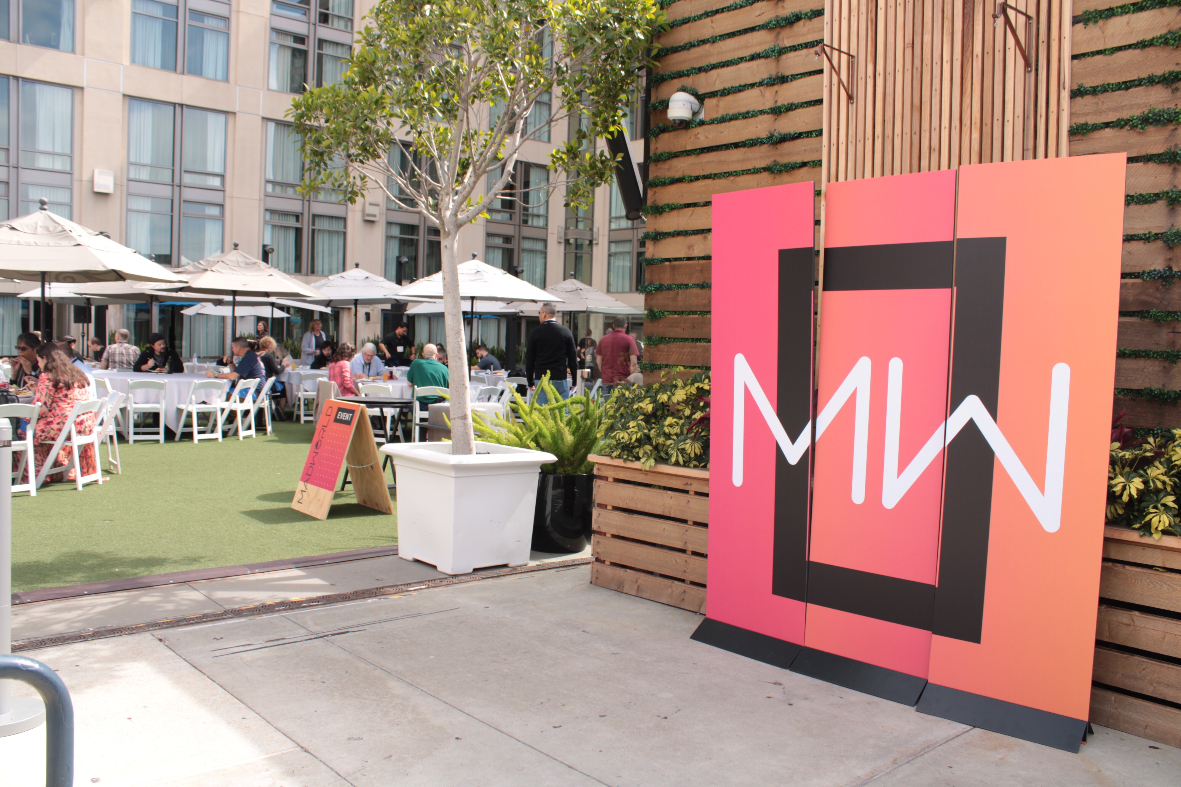 Orange MadWorld sign on rooftop near lunch tables on the grass