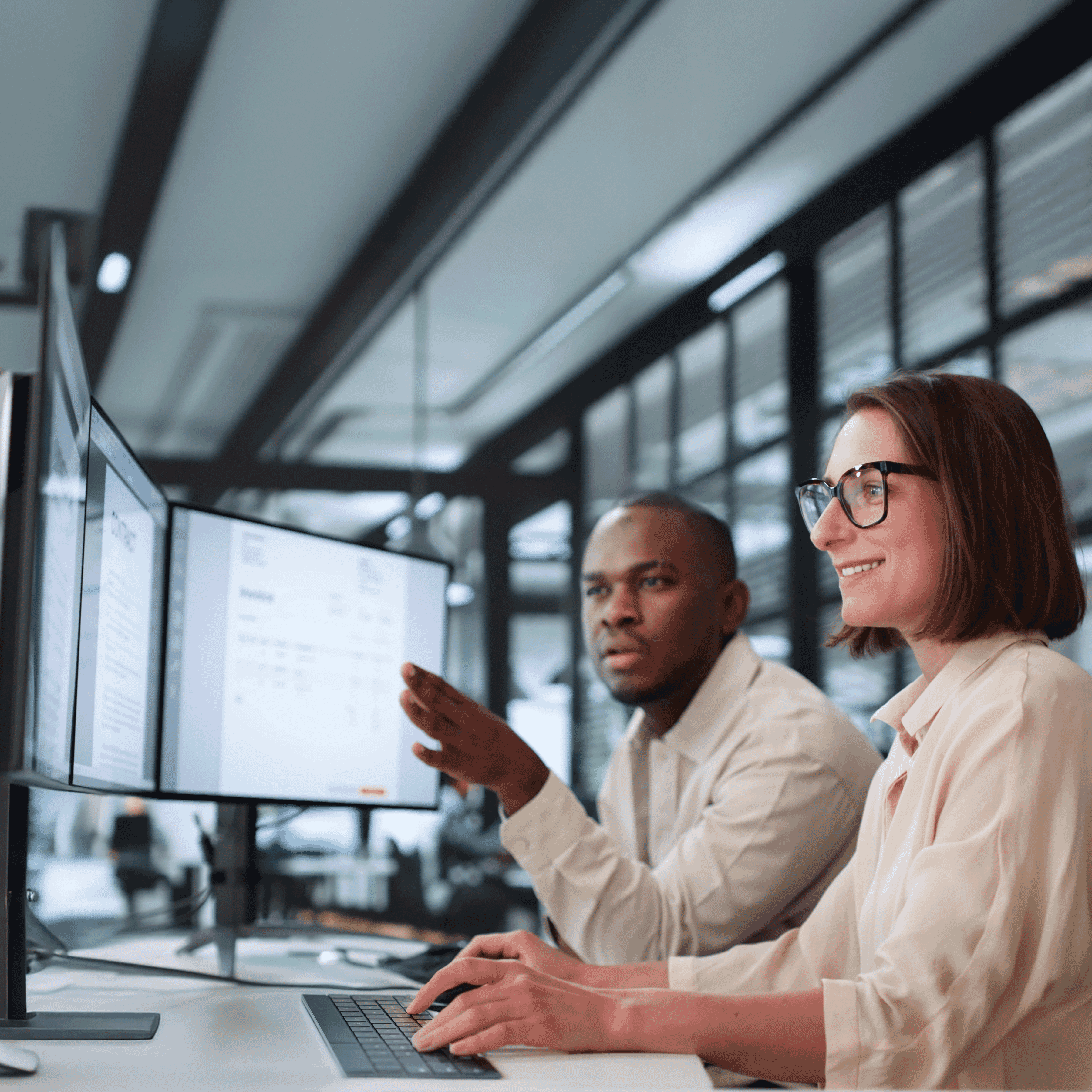 Sitting at a professional tech workspace with dual-monitor set, two technical writers are reviewing structured documentation.