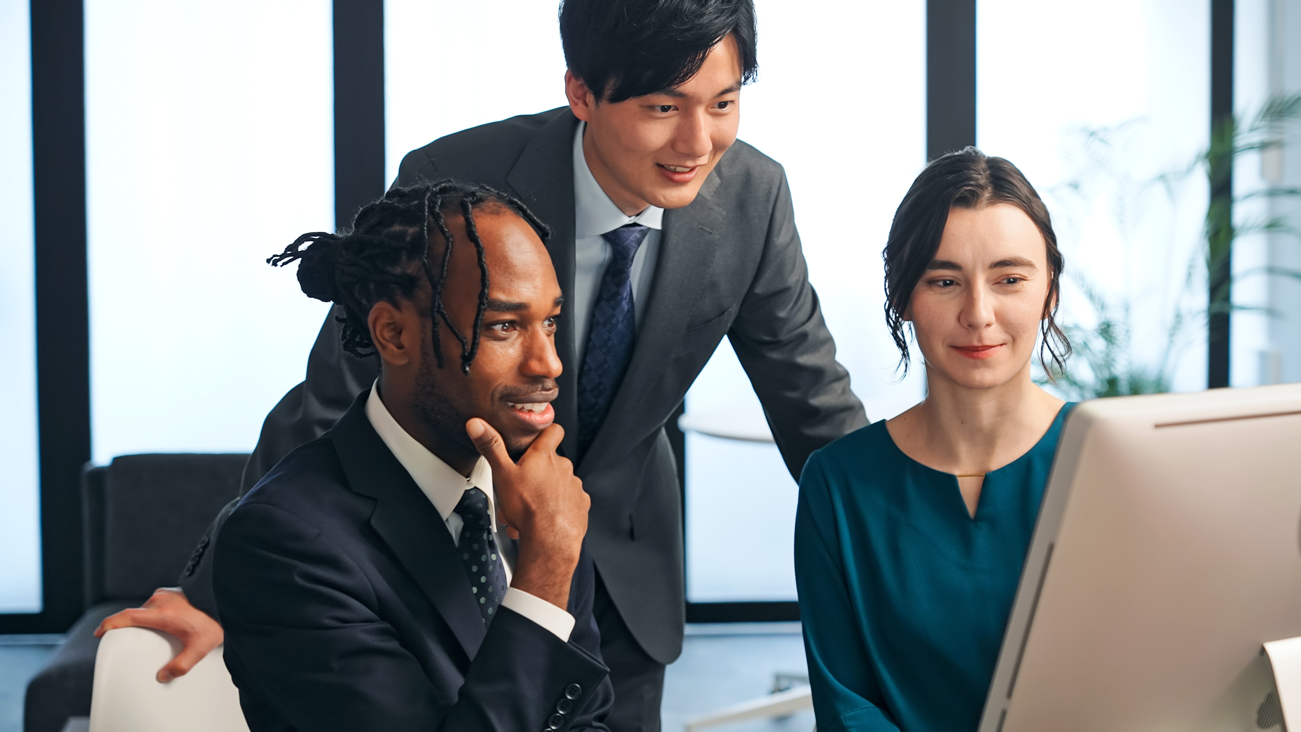 A group of three professionals gathered around a computer monitor in a modern office.