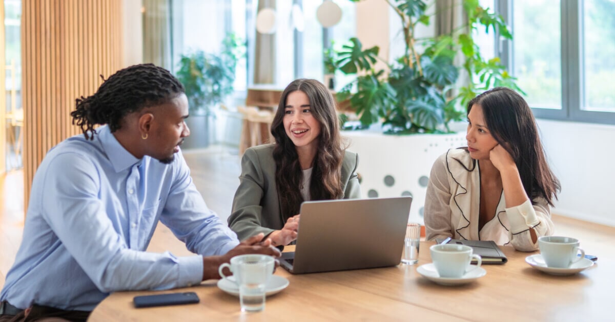 Three professionals gathered around a laptop during a casual business meeting.