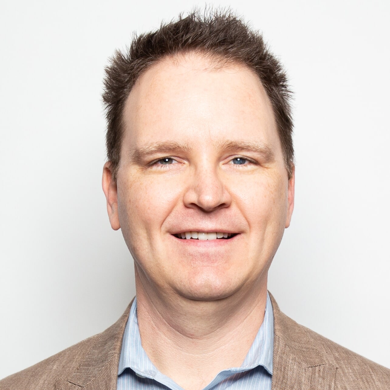headshot of Michael Opsteegh in light blue button up shirt and brown jacket