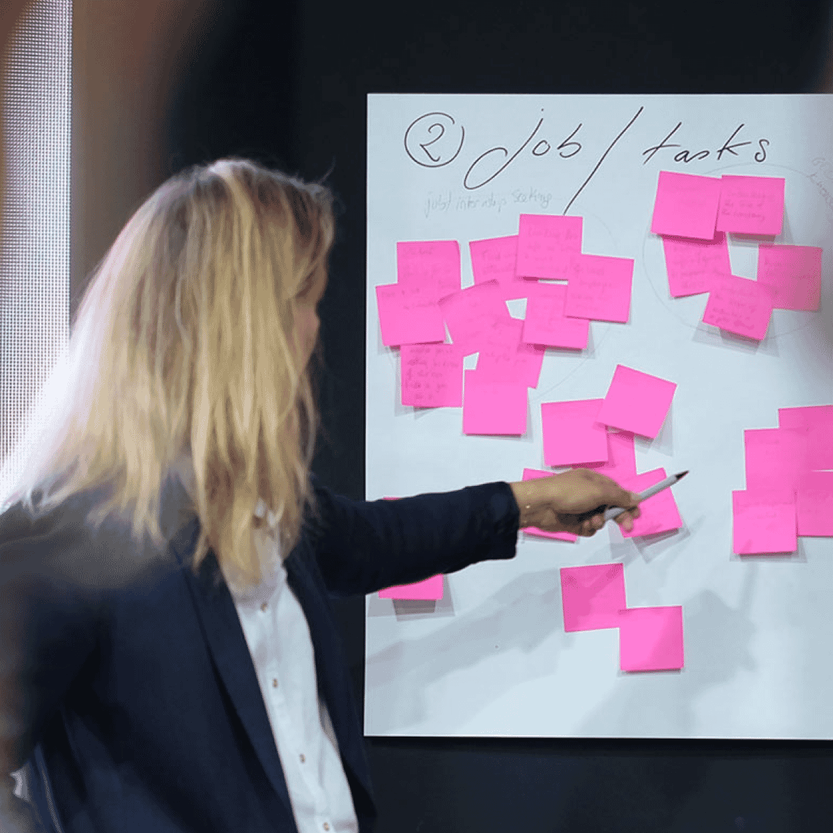 Business woman pointing to poster board covered in pink sticky notes with IXIA Talks logo and Episode 15 description