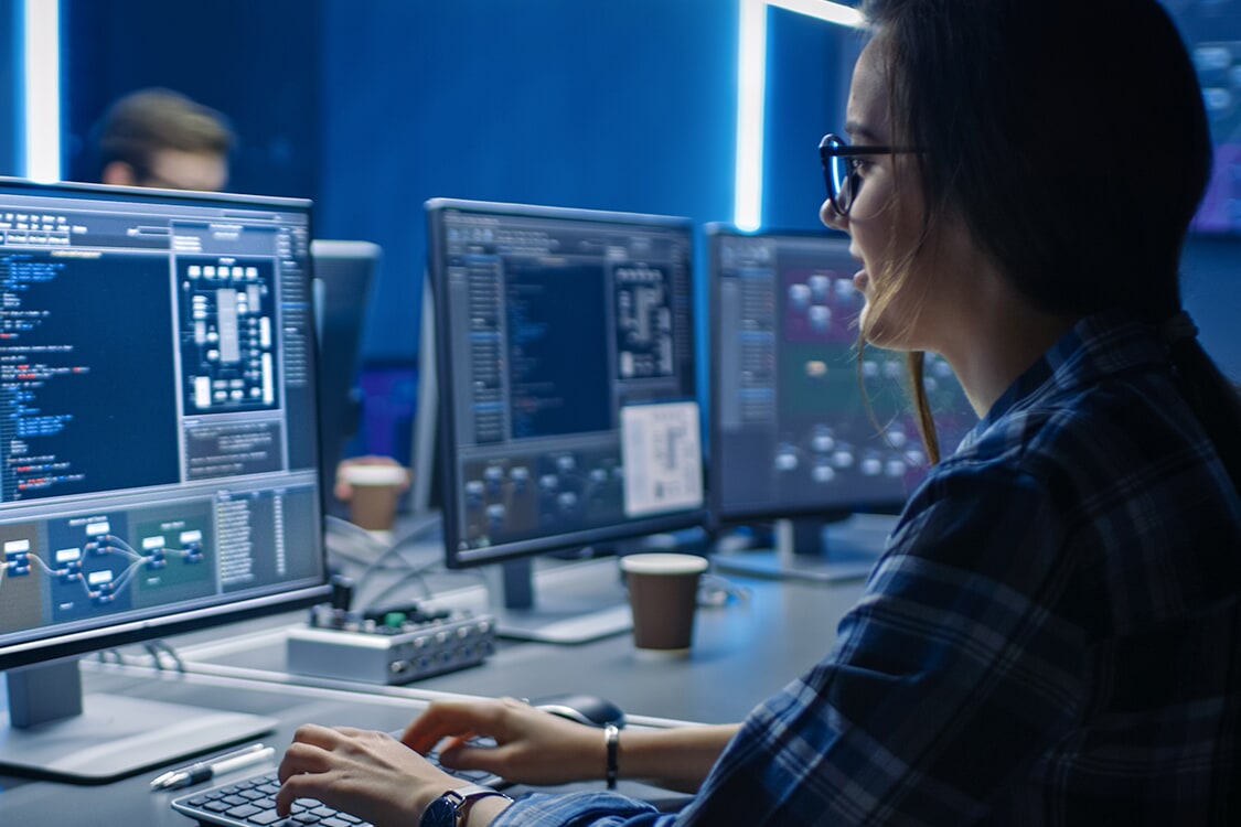 Developer at workstation with multiple monitors showing code