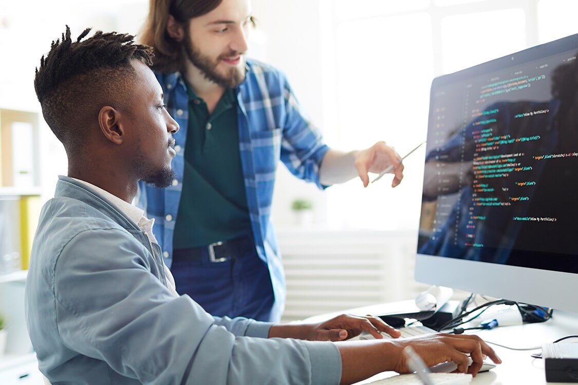 Two developers reviewing colorful code on a large monitor in a bright office