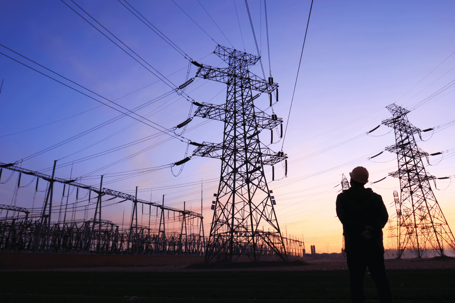 Worker silhouetted against power transmission towers at sunset