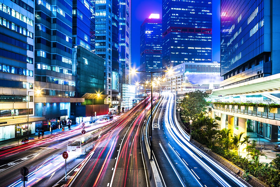 Long-exposure city night view with car light trails between skyscrapers
